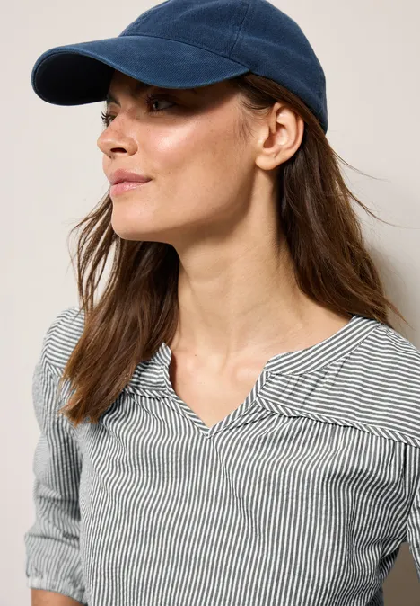 Frau mit blauem Cap und gestreifter Bluse, schaut nach links.